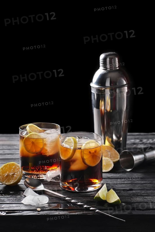 Selective focus composition with rum and cola cocktail served with citrus on rough paper and fabrick over the wooden table with pieces of ice