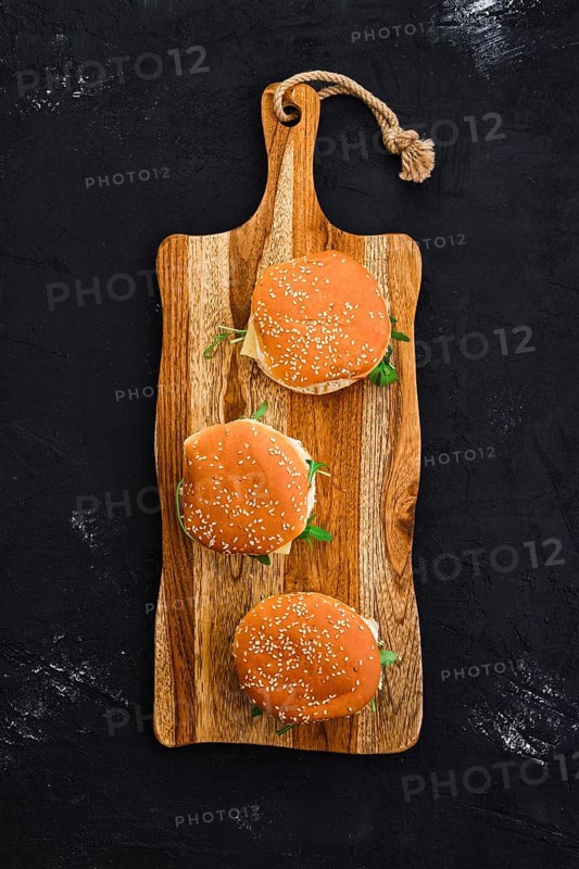 Overhead view of homemade burger with chicken cutlet on long wooden board