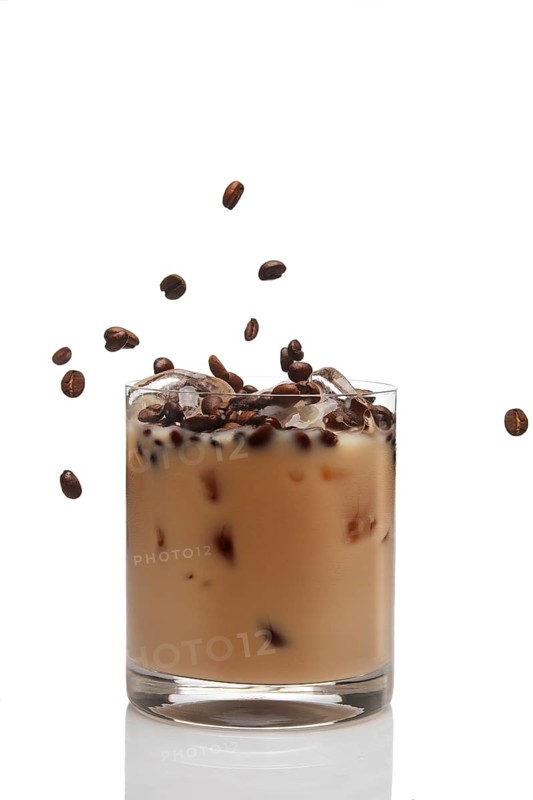 Coffee beans falling into cocktail with Irish creme liqueur in a glass full of ice