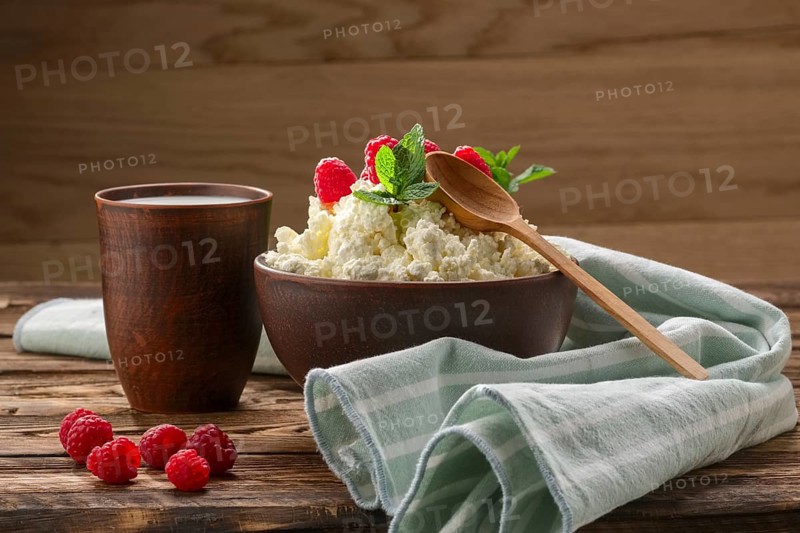 Cottage cheese with wooden spoon on it and milk in clayware on wooden table
