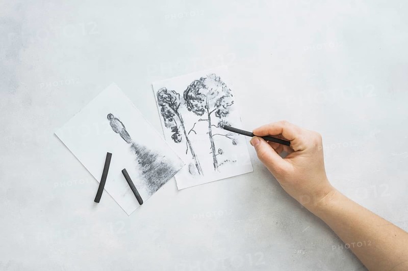 Person s hand sketching beautiful drawing with charcoal stick white surface