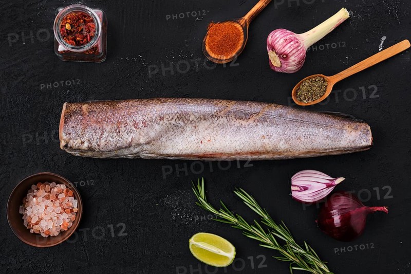 Raw hake with spice on black background