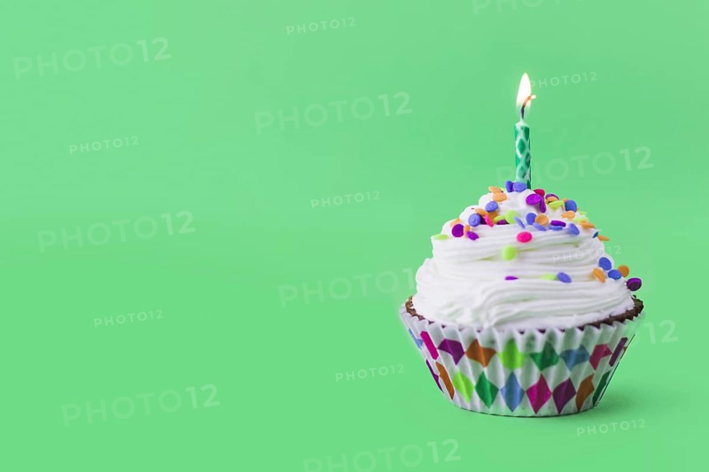 Close up delicious cupcake with burning candle green background