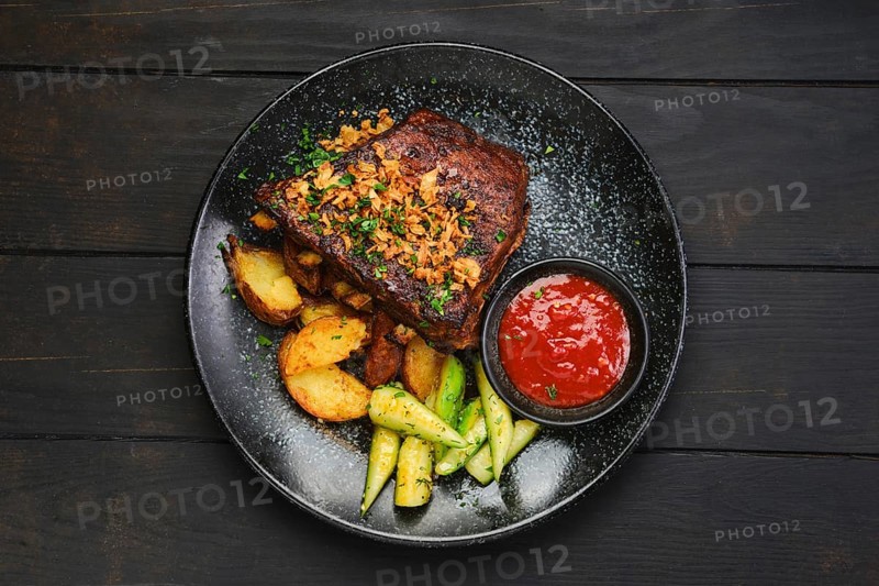 Top view of juicy grilled pork ribs with potato wedges and cucumber