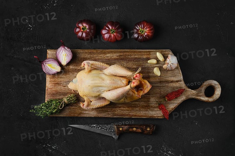 Raw whole chicken with spices on wooden cutting board