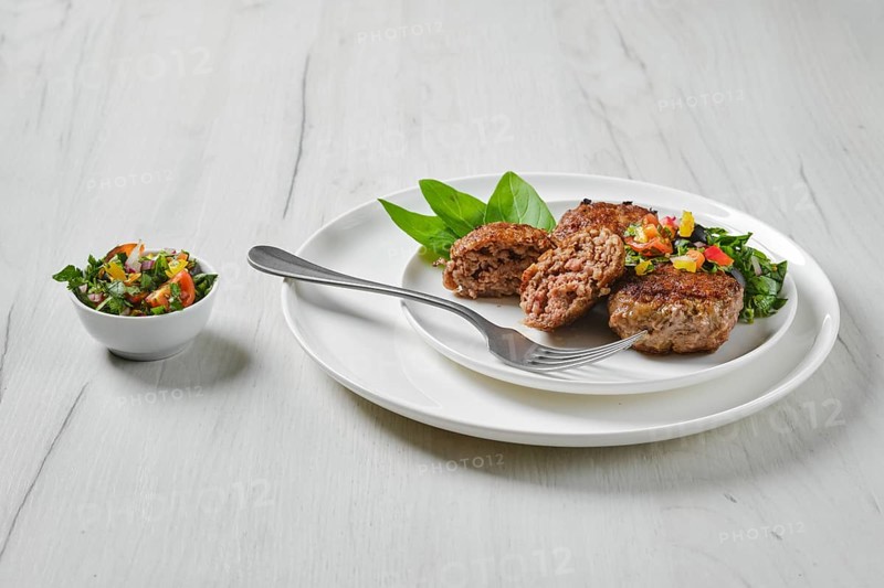Fried veal meatballs on a plate with basil and tomato