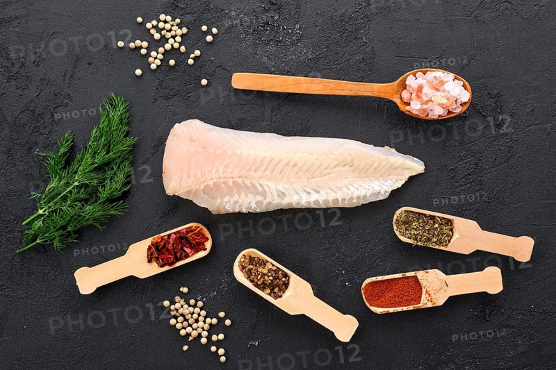 Raw shallow-water hake fillet with spice and herbs on black concrete background