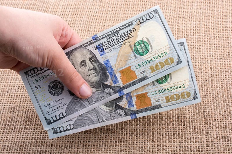 Hand holding banknote bundle of US dollar on a linen canvas background