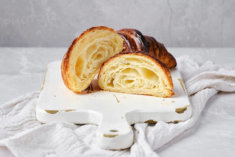 Cross section of classic croissant on marble background and white wooden board