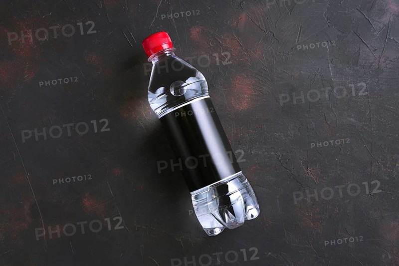 Plastic bottle of water with black label and red cap on table