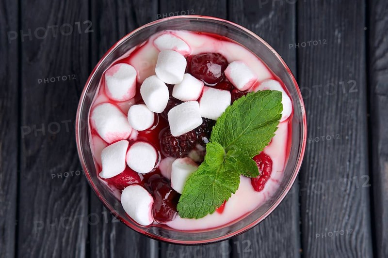 A glass of youghurt with marshmallow and raspberries decorated with mint leaves. Top view
