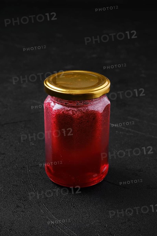 Whole closed jar of cherry jam on black background