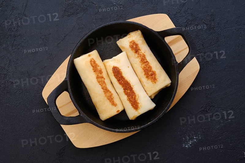 Top view of thin pancakes stuffed with turkey meat in cast iron skillet
