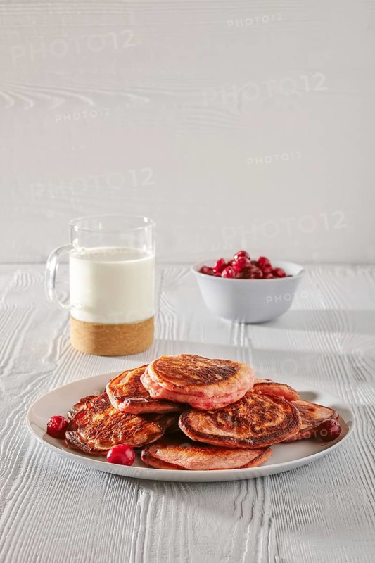 Pancakes with cherry and glass of milk on white kitchen table