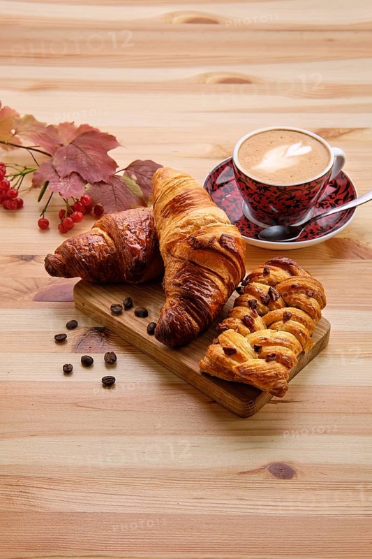 Puff pastry raisin bun and crispy croissant on wooden table with coffee