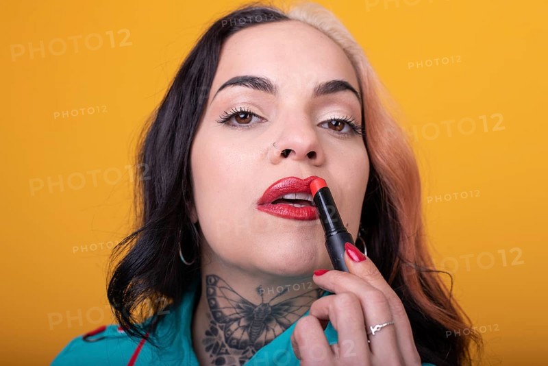Beautiful caucasian woman applying a bright red color lipstick on her lips over yellow background