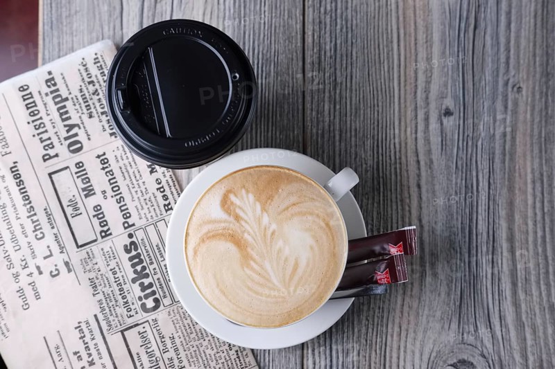 Ceramic and cardboard cup of coffee on wooden table near newspaper. Top view