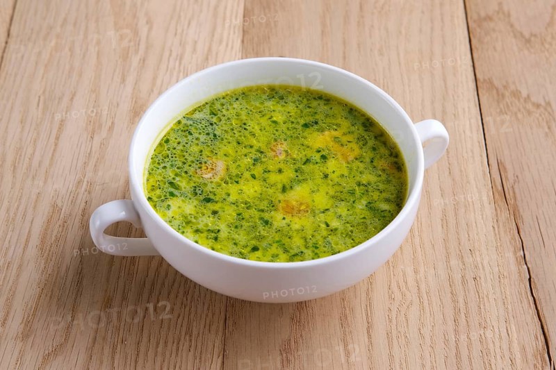 Green soup with asparagus and small sausage on wooden table