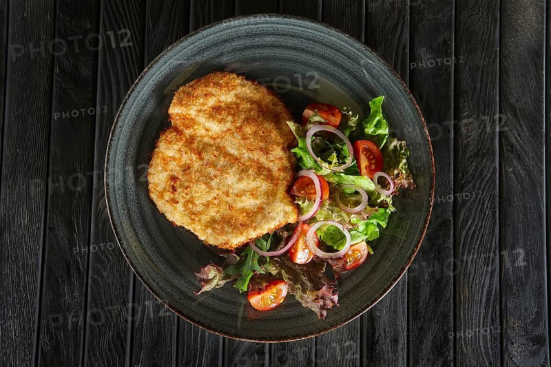 Top view of schnitzel in breading with fresh vegetables and rings of red onion