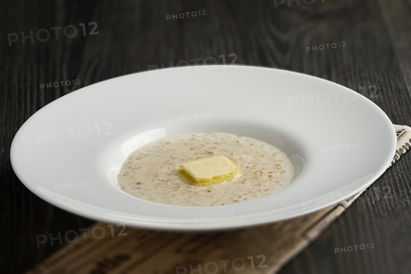 Plate of liquid oatmeal with melting piece of butter on wooden table