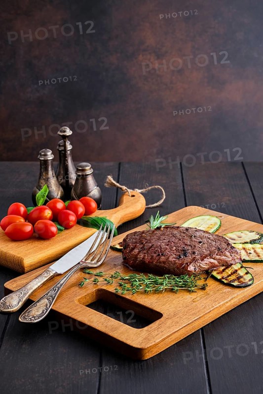 Juicy grilled beef steak and zucchini served with fresh tomato cherry and basil on wooden cutting board