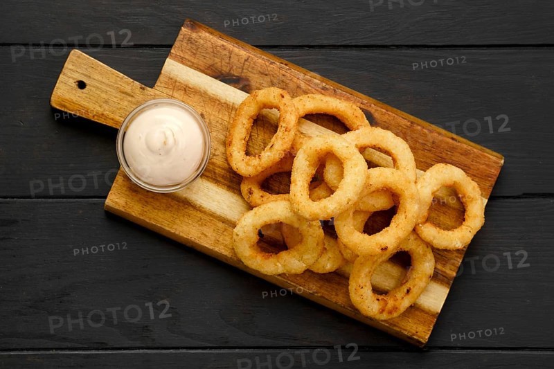Top view of deep fried breaded squid rings with creamy sauce on wooden serving board