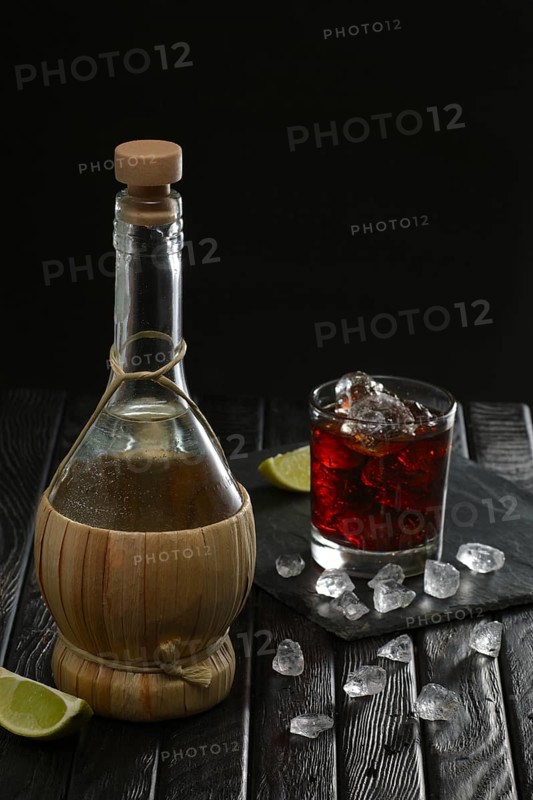 Bottle of homemade vodka and cold cocktail with lime and coffee liquor on dark background