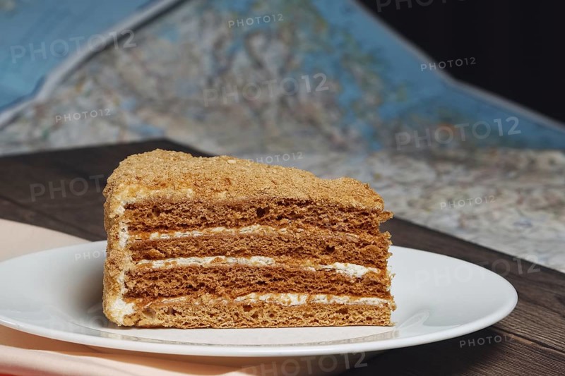Piece of honey cake on plate near map on the table