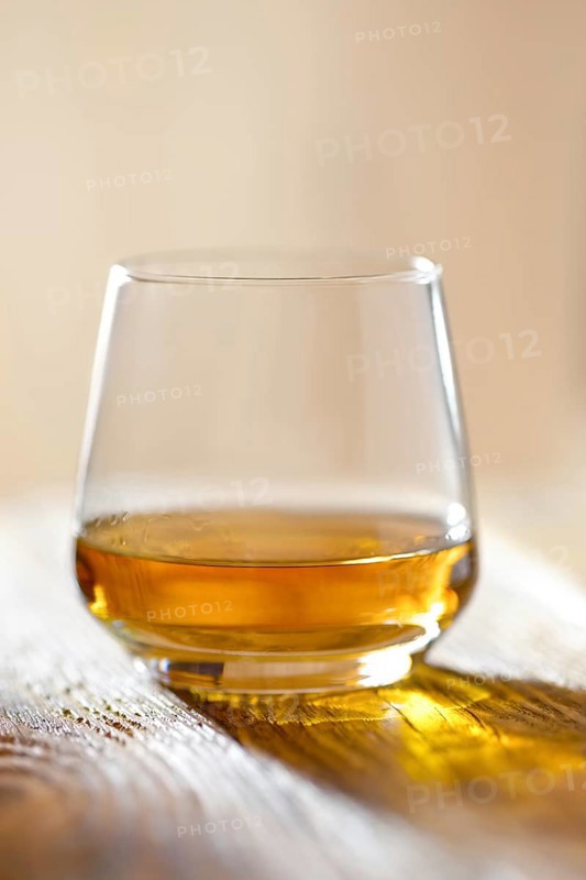 Sniffer glass with whiskey on wooden table in sunlight with hadsh shadow