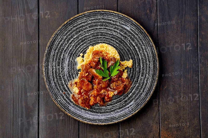 Beef goulash with millet porridge and creamy sauce on dark wooden table