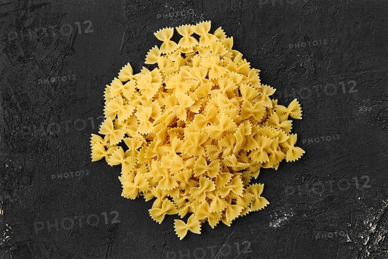 Top view of raw farfalle pasta with spice and herbs on black background