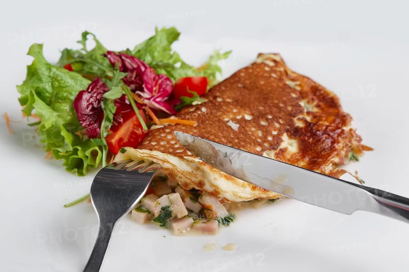 Cutting with knife omelet with ham and fresh vegetables