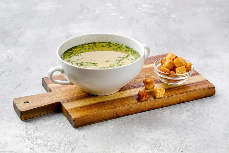 Chicken stock with croutons on wooden serving board