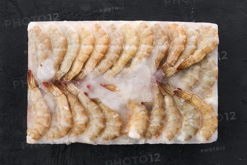 Raw tiger shrimp frozen in large ice cube on black concrete background