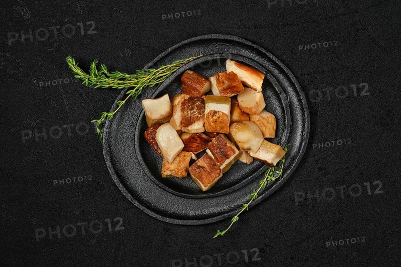Overhead view of frozen fresh boletus cut on pieces on black stone plate
