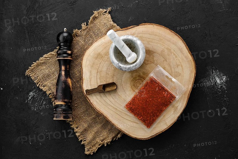 Wooden cross section with paprika in plastic package and stone mortar and mill