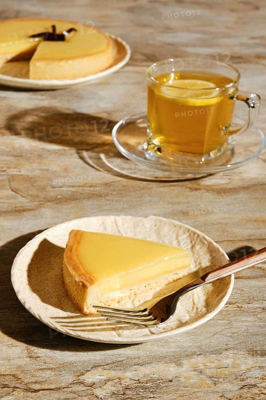 Piece of lemon tart with tea under direct sunlight with hard shadows on the table