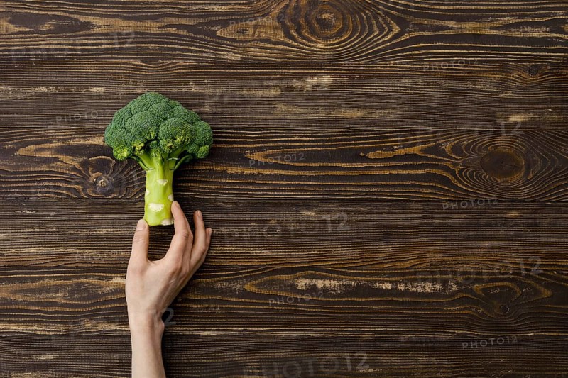 Overhead view of fresh broccoli in hands over wooden background