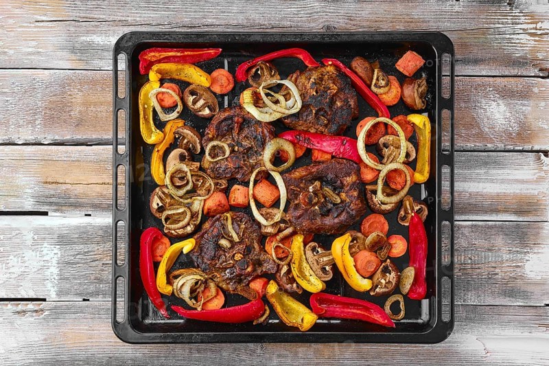 Lamb neck with champignon and vegetables baked in oven on wooden table