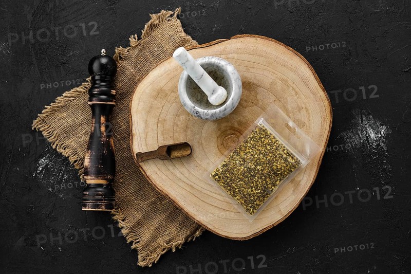 Wooden cross section with lemon pepper in plastic package and stone mortar and mill