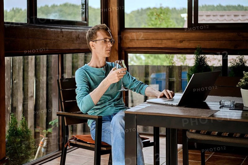 Middle aged man drinking wine and chatting in messenger on laptop
