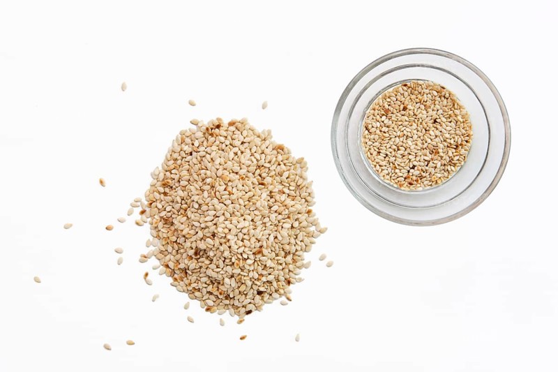 Top view of sesame seeds in a little dish and spilled on white background