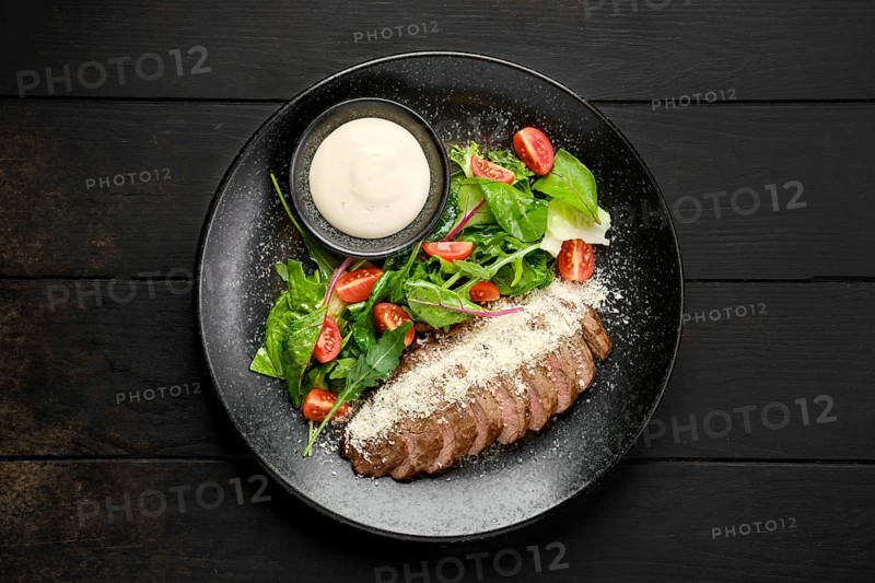 Top view of sliced beefsteak with parmesan and fresh vegetables