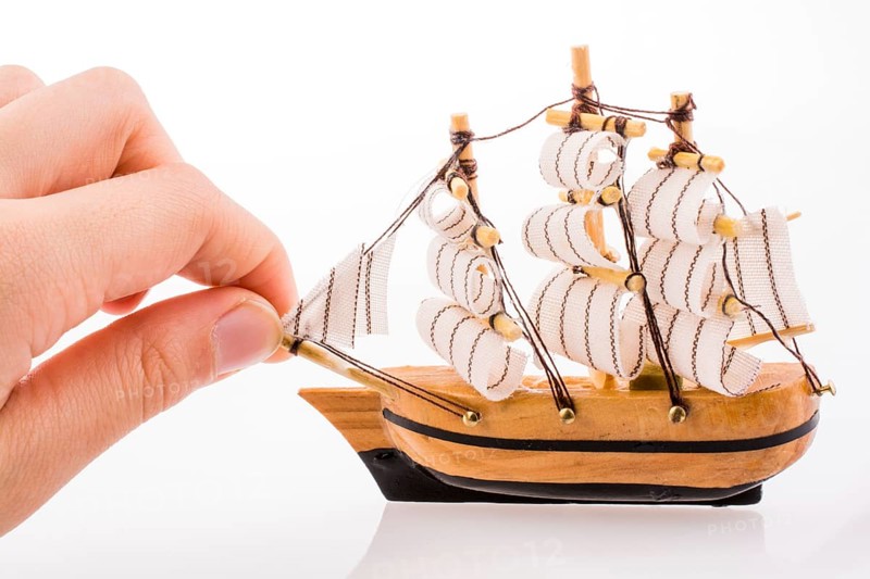 Hand in touch with a little model sailboat on a white background