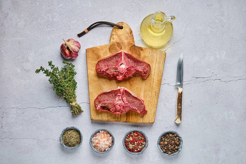 Overhead view of raw fresh deer backstrap with spice and herb over concrete background