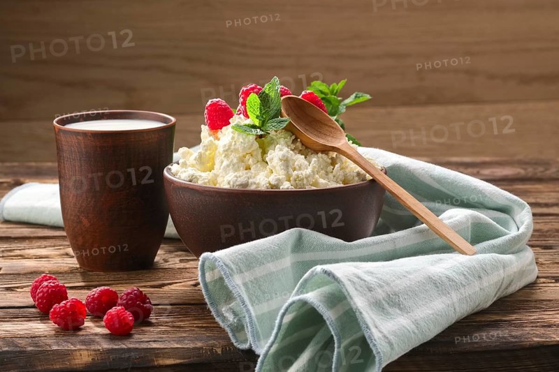 Cottage cheese with wooden spoon on it and milk in clayware on wooden table