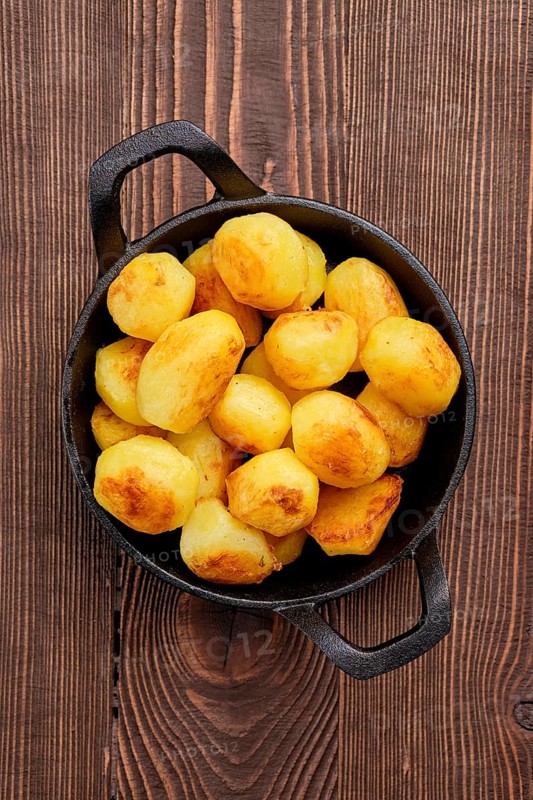 Top view of baked potato in cast iron skillet on natural wooden background