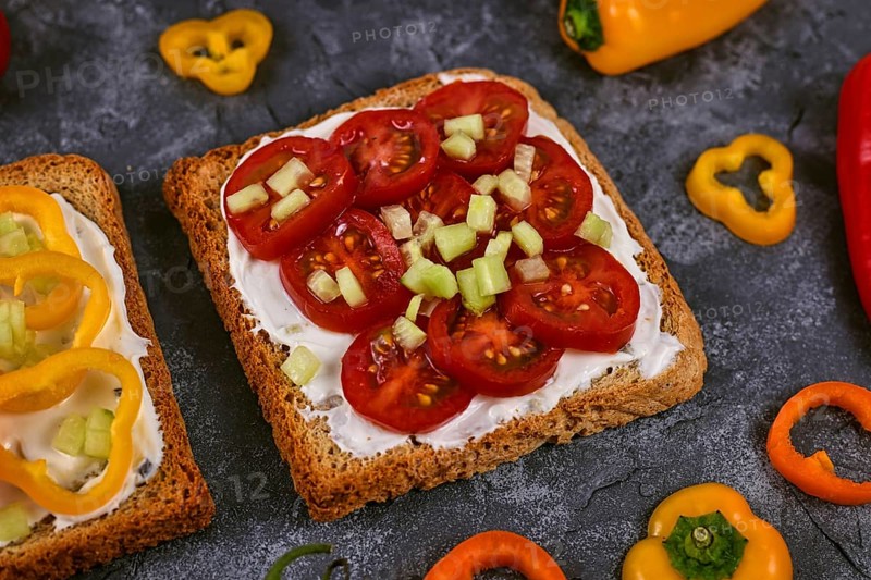 Slice of healthy whole grain toast topped with vegetables like red cherry tomatoes and cucumber pieces