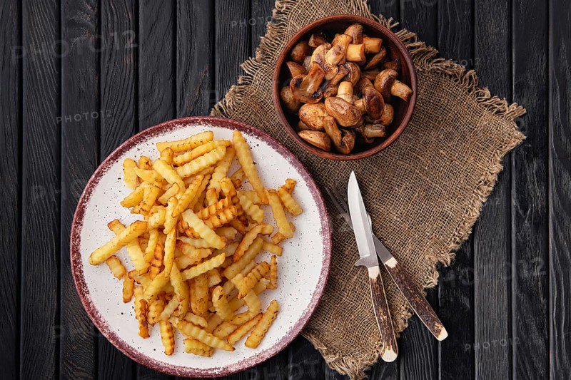 Fried crinkle cut american fries and roasted mushrooms on dark wooden table