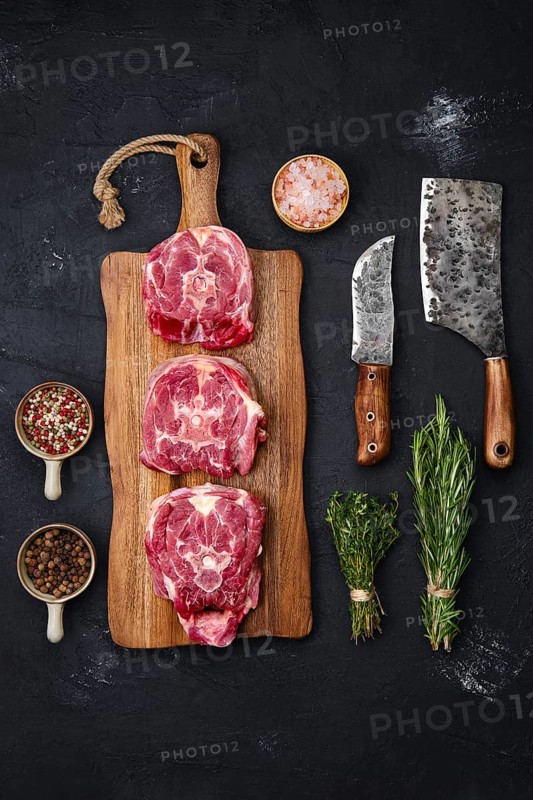 Fresh raw lamb neck on wooden cutting board with herbs and seasoning